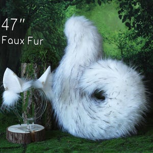 Puede incluir: Una cola de piel sintética blanca y gris, de aproximadamente 120 cm de largo, y un juego de orejas a juego. La cola es rizada y esponjosa, y las orejas están montadas en una diadema transparente. El texto "47" y "Faux Fur" es visible.