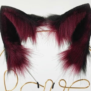 May include: A pair of black and burgundy cat ears made of faux fur. The ears are attached to a headband.
