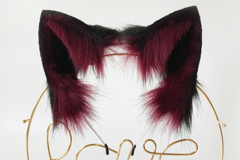 May include: A pair of black and burgundy cat ears made of faux fur. The ears are attached to a headband.
