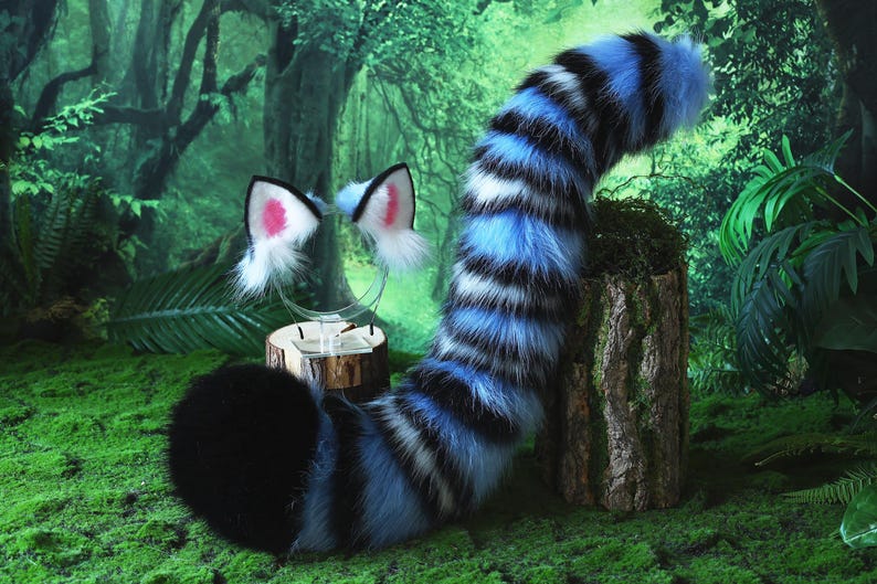 May include: A furry costume set featuring a black and blue striped tail and matching cat ears with pink inner ears. The tail is long and curved, and the ears are attached to a clear headband. The set is designed for cosplay or costume use.