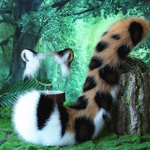 May include: A fluffy, brown, black, and white cat tail with a spotted pattern. The tail is curled up and appears to be made of faux fur. The tail is in front of a green and brown background.