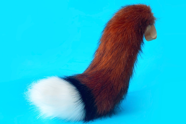 Puede incluir: Una cola de piel sint&eacute;tica roja y negra, con una punta blanca. La cola est&aacute; enroscada y tiene una base de fieltro marr&oacute;n.