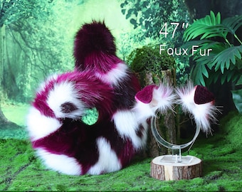 May include: A faux fur tail, approximately 47 inches long, in a pattern of white, burgundy, and black. A matching headband with ear accents is also visible. The items are displayed on a mossy surface.