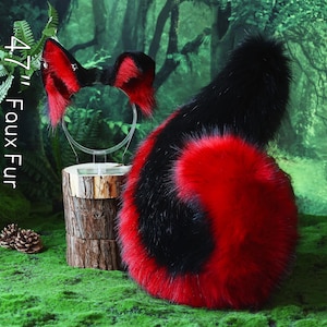 Puede incluir: Un conjunto de cola y diadema de orejas de piel sintética roja y negra. La cola es un remolino de rojo y negro, y las orejas son rojas con puntas negras. El texto "47" Faux Fur" es visible.