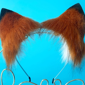 Puede incluir: Una diadema con orejas de zorro de piel marr&oacute;n y puntas blancas. La diadema es de metal y est&aacute; sobre un fondo azul.