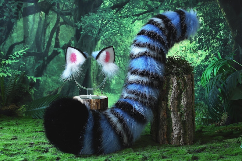 May include: A furry costume set featuring a black, blue, and white striped tail and matching cat ears with pink inner ear details. The tail is thick and curved, and the ears are attached to a silver headband. The set is designed for cosplay or costume use.
