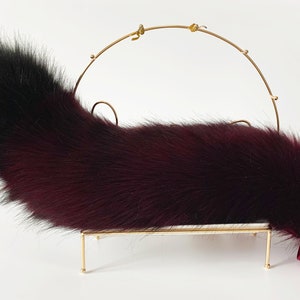 May include: A burgundy and black faux fur tail with a gold metal stand and a red ribbon.