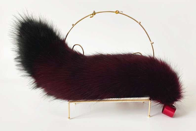 May include: A burgundy and black faux fur tail with a gold metal stand and a red ribbon.