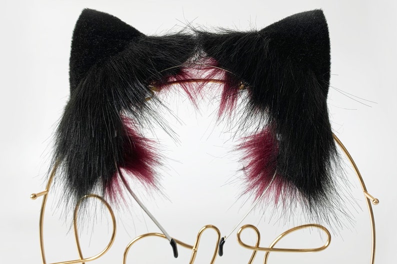 May include: Black cat ears headband with burgundy tips. The headband is made of faux fur and is attached to a metal headband.