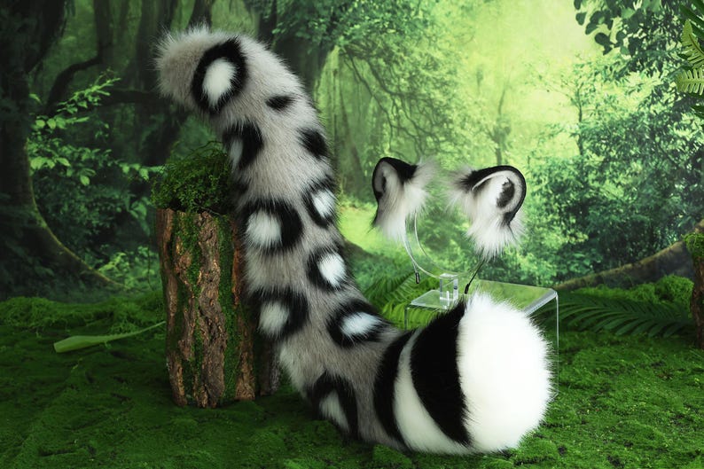 May include: A white and black spotted faux fur tail with a white tip. The tail is attached to a black and white spotted faux fur headband with large ears.