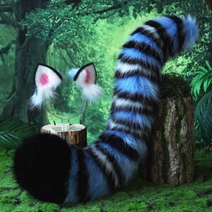 May include: A furry costume set featuring a black and blue striped tail and matching cat ears with pink inner ears. The tail is propped up on a wooden stump against a backdrop of a lush green forest.