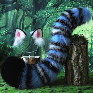 May include: A furry costume tail and cat ear headband set. The tail is blue, black, and white striped, and the ears are white with pink inner ears. The items are displayed on a mossy surface with a forest backdrop.