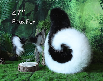 May include: A black and white faux fur tail and matching ear headband set. The tail is 47 inches long. The ears are black and white. The items are displayed on a green surface with a forest backdrop.