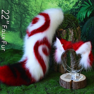 Op de afbeelding: Een 56 cm lange faux fur staart en bijpassende oorbandsset. De staart is wit met rode en zwarte wervelingen. De oorband is rood en wit. De set wordt gepresenteerd op een mosachtig oppervlak.