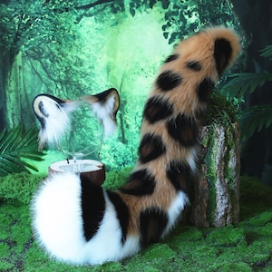 May include: A brown, black, and white faux fur tail with a spotted pattern. The tail is curled up and is sitting on a green mossy surface.