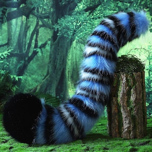 May include: A plush, blue, black, and white striped tail prop, likely for cosplay or costume use, rests on a moss-covered tree stump. The tail is set against a backdrop of a lush, green forest, creating a whimsical scene.