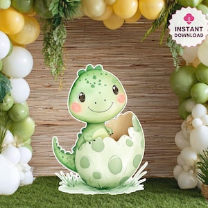 May include: A charming, green dinosaur emerging from an egg, with a smiling face and pink cheeks. The dinosaur is a cutout, set against a backdrop of balloons and greenery. The words "Instant Download" are in a pink circle.