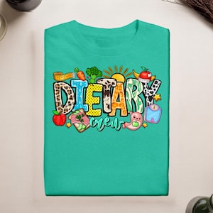 May include: A teal t-shirt featuring a graphic print with the text "DIETARY crew". The letters are filled with various patterns including leopard print, cow print, and polka dots. Surrounding the text are illustrations of food and health items.
