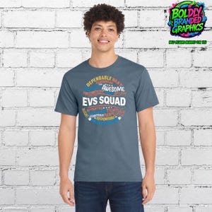 May include: A slate blue short-sleeve t-shirt featuring a circular graphic design with the text EVS SQUAD in large white letters, surrounded by smaller words including DEPENDABLE, BEST, AWESOME, TRUSTWORTHY, EFFICIENT, SUPPORTIVE, THOROUGH, and RESPECTFUL.