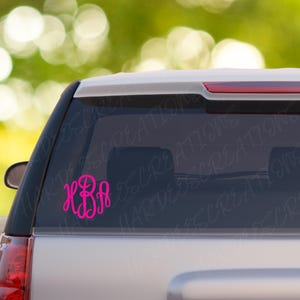 May include: A hot pink monogram decal, featuring the letters KBA in a cursive font, is affixed to the rear window of a silver vehicle. The decal is a circular design, perfect for personalizing cars, laptops, or other items.
