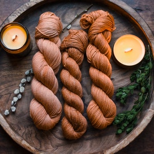 May include: Three skeins of orange yarn on a wooden tray with two lit candles. The yarn is arranged in a spiral pattern.