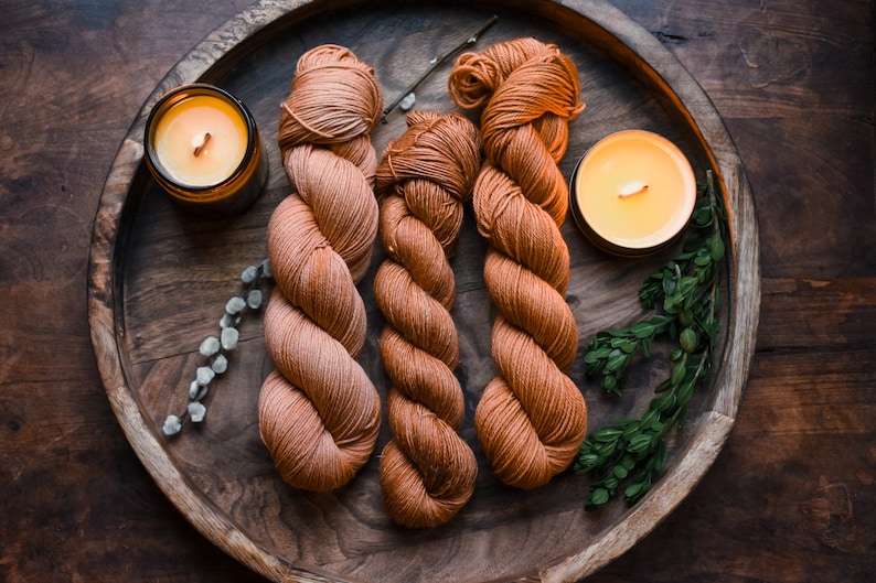 May include: Three skeins of orange yarn on a wooden tray with two lit candles. The yarn is arranged in a spiral pattern.