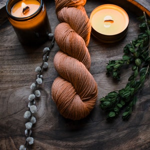 May include: A skein of orange yarn, two lit candles, and a sprig of green foliage on a wooden tray.