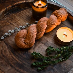 May include: A wooden tray with a ball of orange yarn, two lit candles, a sprig of green foliage, and a branch of pussy willow.