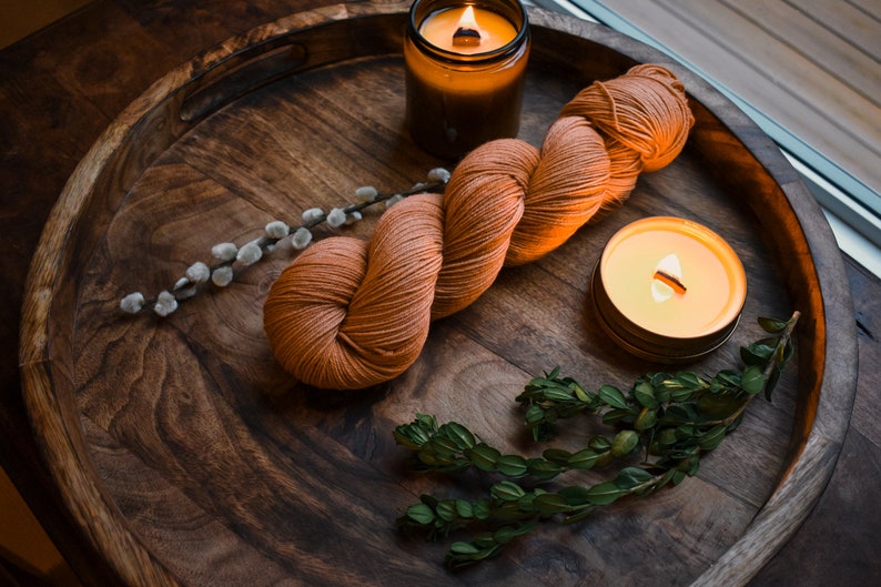 May include: A wooden tray with a ball of orange yarn, two lit candles, a sprig of green foliage, and a branch of pussy willow.