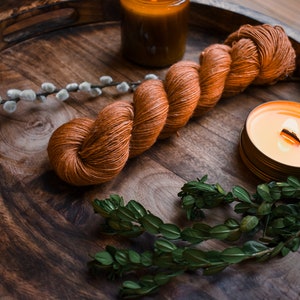 May include: A wooden tray with a skein of orange yarn, a lit candle, and sprigs of greenery.