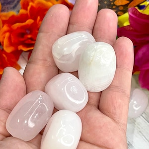 May include: A collection of six polished, oval-shaped stones in varying shades of pink and white. The stones are smooth and appear to be tumbled. The image is a close-up, showcasing the stones' textures and colors.