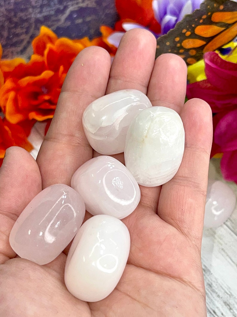 May include: A collection of six polished, oval-shaped stones in varying shades of pink and white. The stones are smooth and appear to be tumbled. The image is a close-up, showcasing the stones' textures and colors.