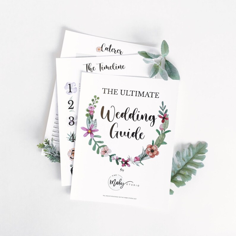 May include: A printable wedding guide with a floral wreath design. The guide includes sections for the caterer, timeline, and other wedding planning details. The text reads "The Ultimate Wedding Guide by The Maby Studio."