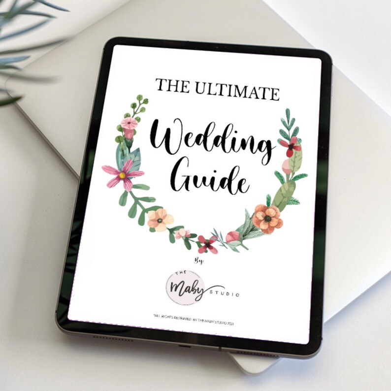 May include: A digital tablet displaying a wedding guide with a floral wreath design. The text reads "The Ultimate Wedding Guide" and "The Maby Studio".
