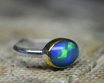 May include: A silver ring with a gold setting and a blue and green opal gemstone.