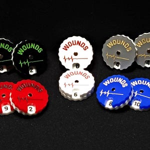 May include: Set of ten round plastic wound trackers with a heartbeat graphic and the word "Wounds" printed on each. The trackers are in various colours, including black, white, red, blue, and grey. Each tracker has a number from 1 to 10 printed on it.