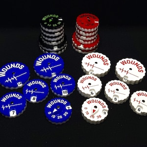 May include: A collection of 12 blue, white, and red plastic wound counters with a heartbeat symbol and numbers. The counters are used for board games and role-playing games.