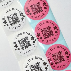 May include: A sheet of round stickers with a pink and white background. The stickers have a black and white QR code and the text "Buy the Bride a drink!" printed on them.