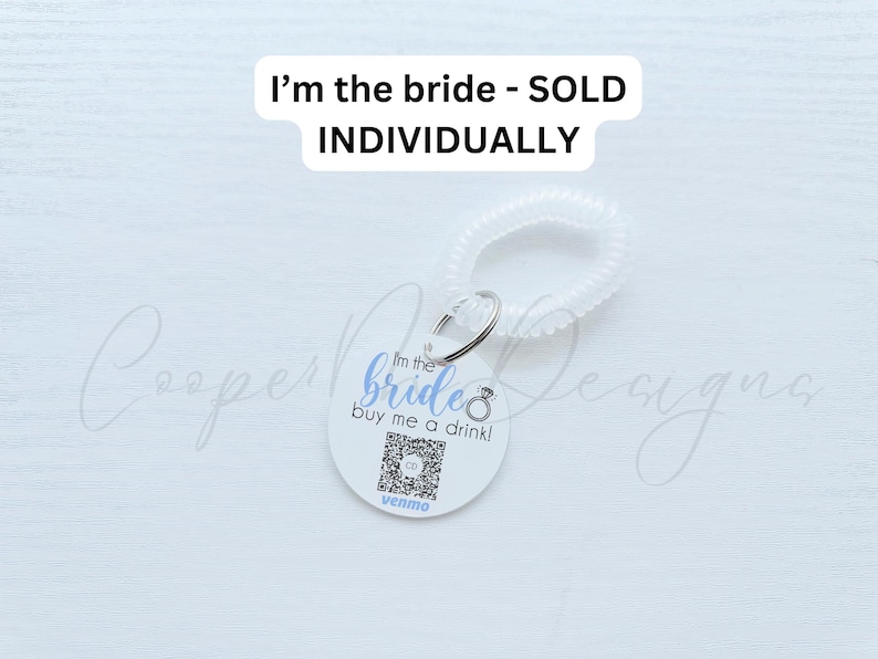 May include: A white round tag with the text "I'm the bride buy me a drink!" in blue and a ring icon. The tag is attached to a white plastic hair scrunchie. The text "I'm the bride - SOLD INDIVIDUALLY" is written in black at the top of the image.
