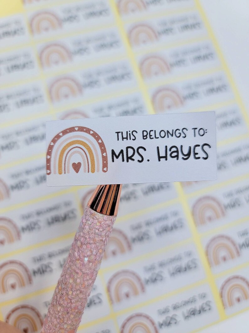 May include: A sheet of white labels with a rainbow design and the text "This belongs to: MRS. HAYES". The labels are on a yellow background.