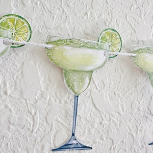 May include: A white string garland with green lime slices and green and white margarita glasses. The garland is perfect for a summer party or a fiesta.