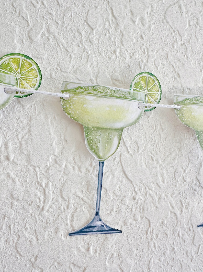 May include: A white string garland with green lime slices and green and white margarita glasses. The garland is perfect for a summer party or a fiesta.