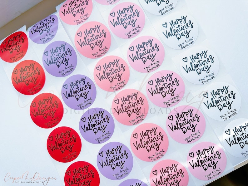 Puede incluir: Surtido de pegatinas redondas para el D&iacute;a de San Valent&iacute;n con el texto "Happy Valentine's Day" en fuente de letra cursiva negra. Las pegatinas est&aacute;n sobre un fondo blanco y vienen en varios colores, incluyendo rosa, rojo, morado y blanco.