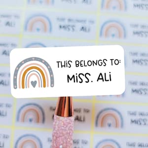 May include: A white sticker with a rainbow design and the text "This belongs to: Miss. Ali" printed on it.