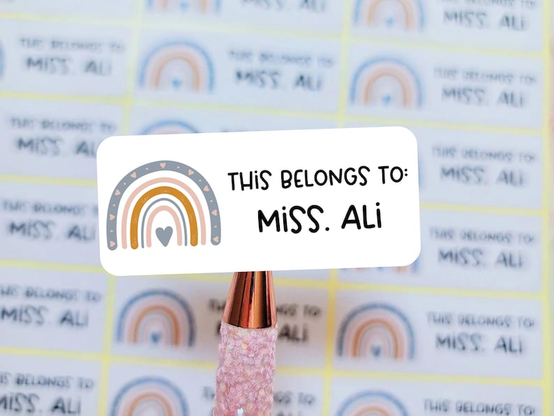 May include: A white sticker with a rainbow design and the text "This belongs to: Miss. Ali" printed on it.