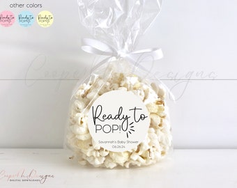 May include: A white favor bag filled with popcorn and a round white sticker with black text that reads "Ready to POP!" and "Savannah's Baby Shower 06.26.24".
