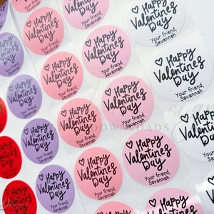 Puede incluir: Una hoja de pegatinas redondas con el texto "Happy Valentine's Day" en escritura cursiva negra. Las pegatinas est&aacute;n sobre un fondo blanco y tienen un fondo rosa, morado o blanco. El texto "Your friend, Savannah" est&aacute; impreso debajo del saludo en cada pegatina.