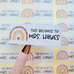 May include: A set of personalized name labels with a rainbow design. The labels feature a rainbow with a heart in the center and the text "This belongs to: MRS. HAYES".