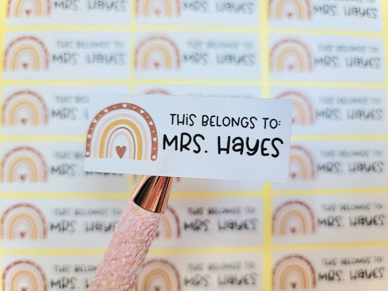 May include: A set of personalized name labels with a rainbow design. The labels feature a rainbow with a heart in the center and the text "This belongs to: MRS. HAYES".
