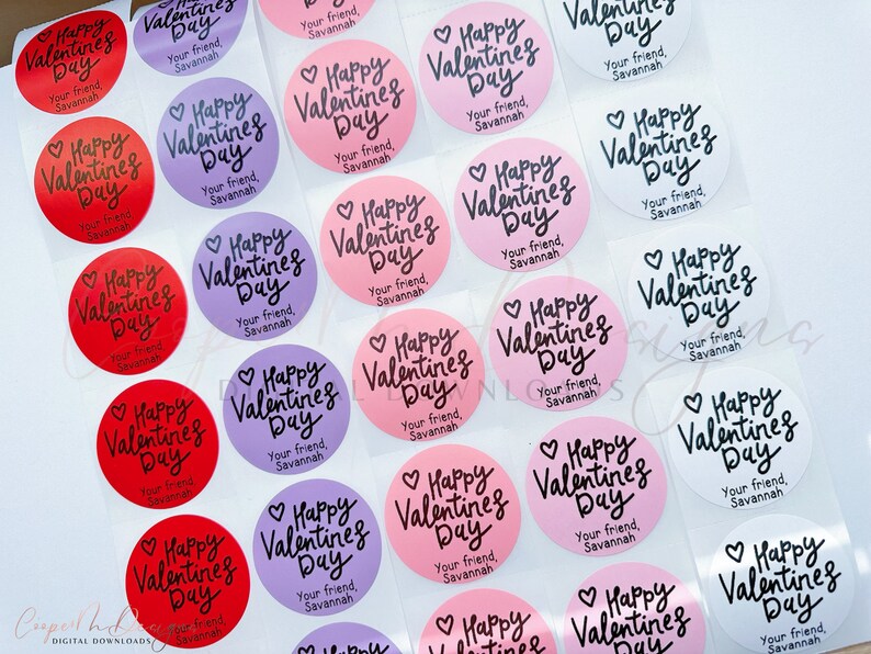 Puede incluir: Una hoja de pegatinas redondas para el D&iacute;a de San Valent&iacute;n con el texto "Happy Valentine's Day" en escritura cursiva negra. Las pegatinas son de varios colores, incluyendo rosa, rojo, blanco y morado. El texto "Your friend, Savannah" est&aacute; impreso en cada pegatina.